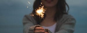 image of a woman in a gray cardigan holding out a sparkler